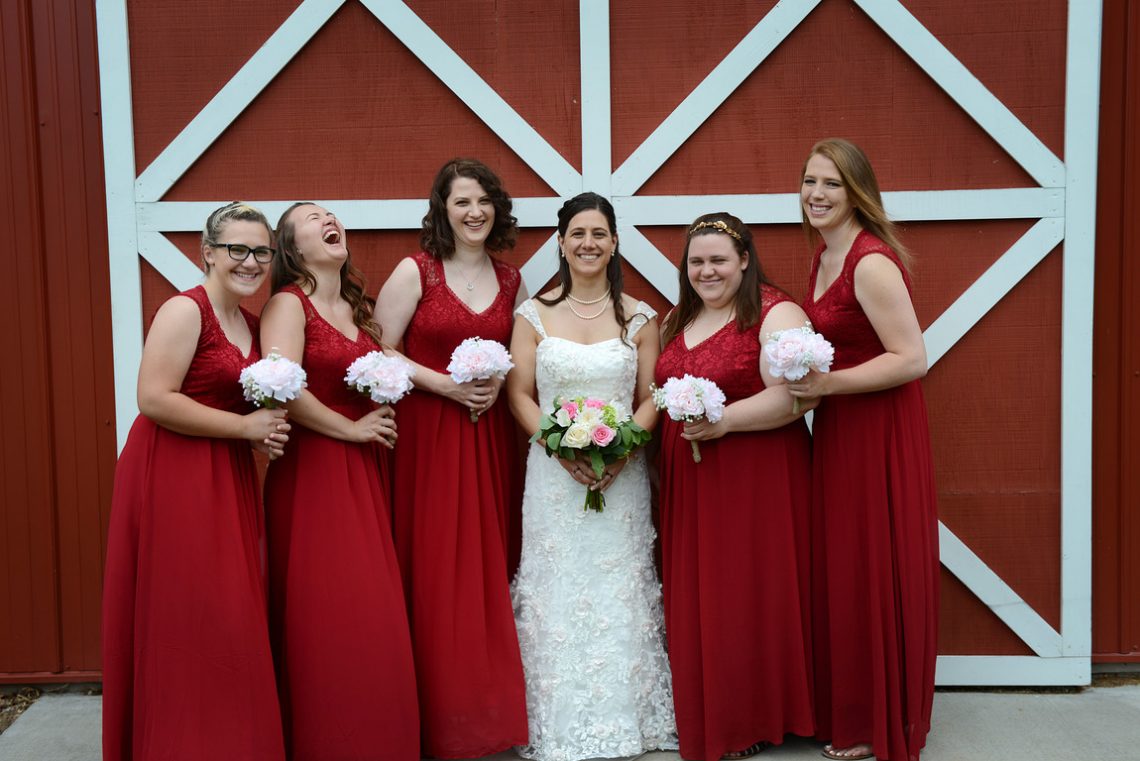Weddings S&T bridesmaid laughing in front of red barn door